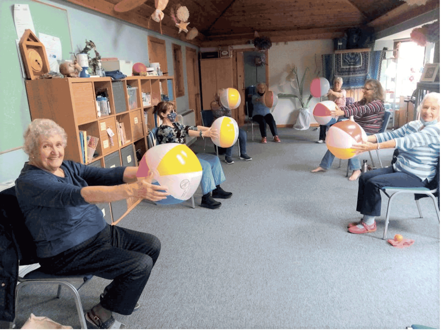 A photograph showing MS Centre Mid Argyll service users during a group activity, holding beach balls in front of them, arms stretched, whilst sitting down.