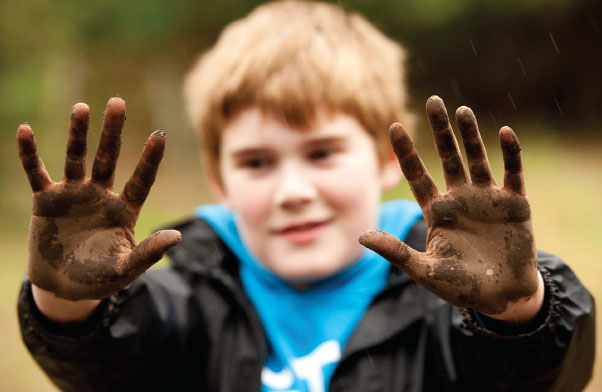 Child holding up both hands which are covered in mud