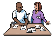 A man in a wheelchair using low tech communication equipment to make decisions. A professional woman is sitting next to him and watching him make his choice.