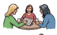 Three women sitting at a table with drinks. One woman is communicating with the others using high-tech communication equipment. All are happy and smiling.
