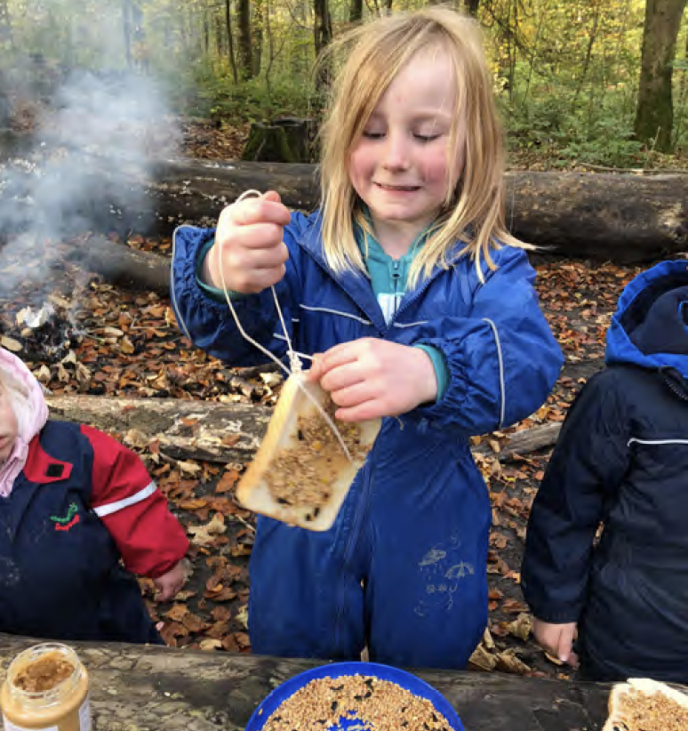 Young child making a bird feeder with a slice of bread, peanut butter and seeds.