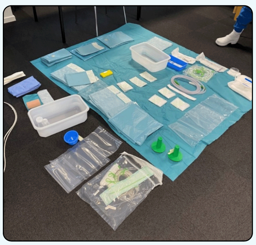 A blue surgical drape on the floor with various single-use equipment - some on the drape and some off the drape