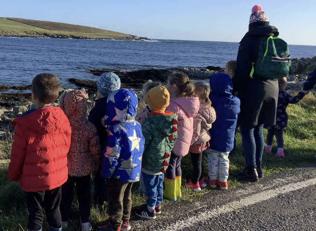 A group of young children with their Early Learning and Childcare practitioner looking out over rockpools to the sea.