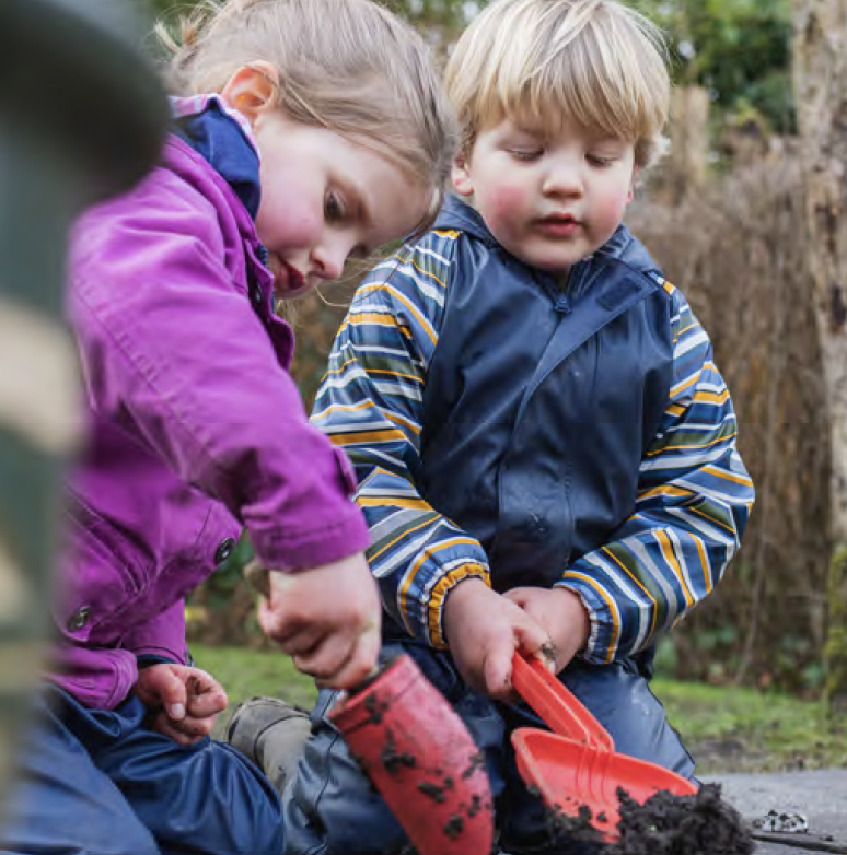 Two young children shovelling soil outdoors.