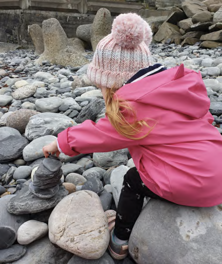Young child carefully stacking rocks by the beach.
