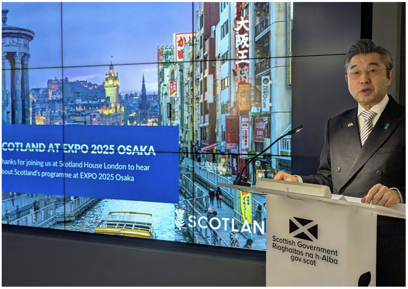 Japanese Ambassador to the UK stands at a podium with the Scottish Government logo. Behind him, a screen displays ‘Scotland at Expo 2025 Osaka’.