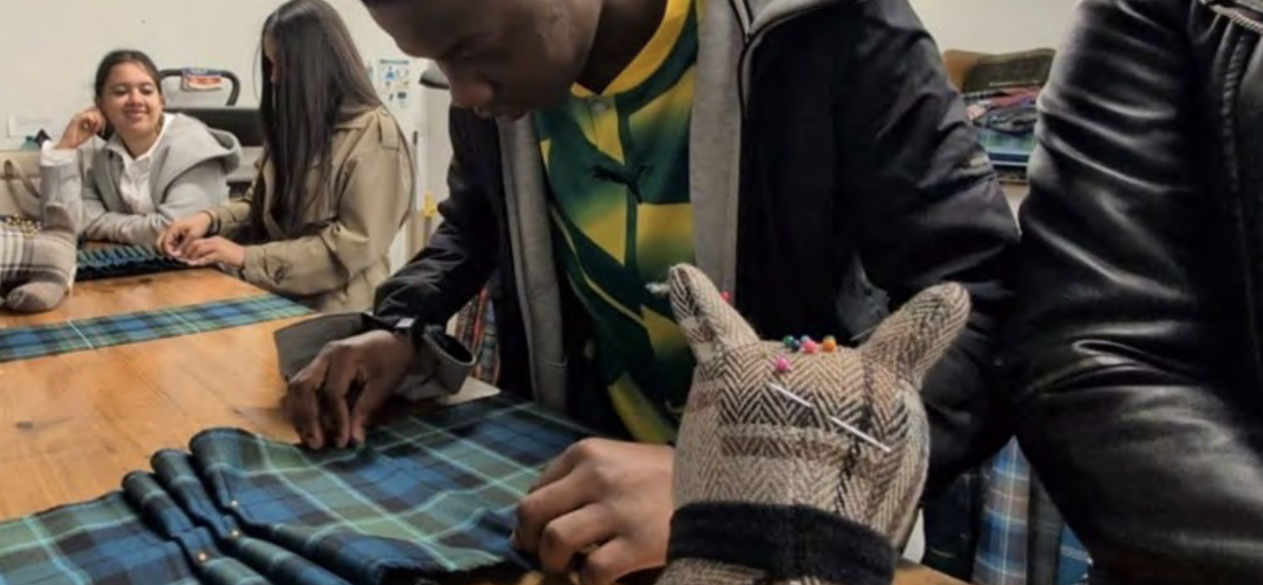 A young student sits around a wooden table in a workshop, crafting with blue tartan.