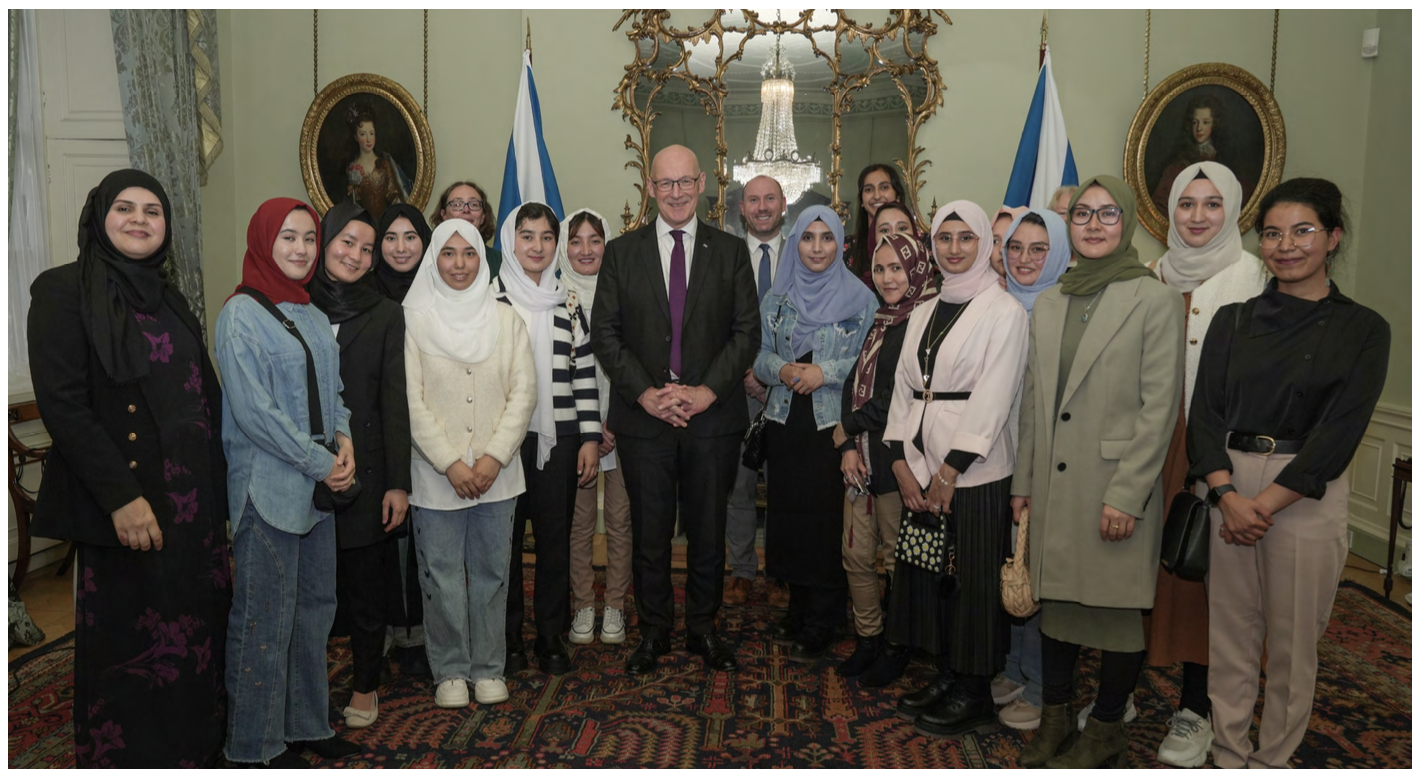 A group of medical students, wearing diverse outfits including headscarves, stand in Bute House with First Minister John Swinney.