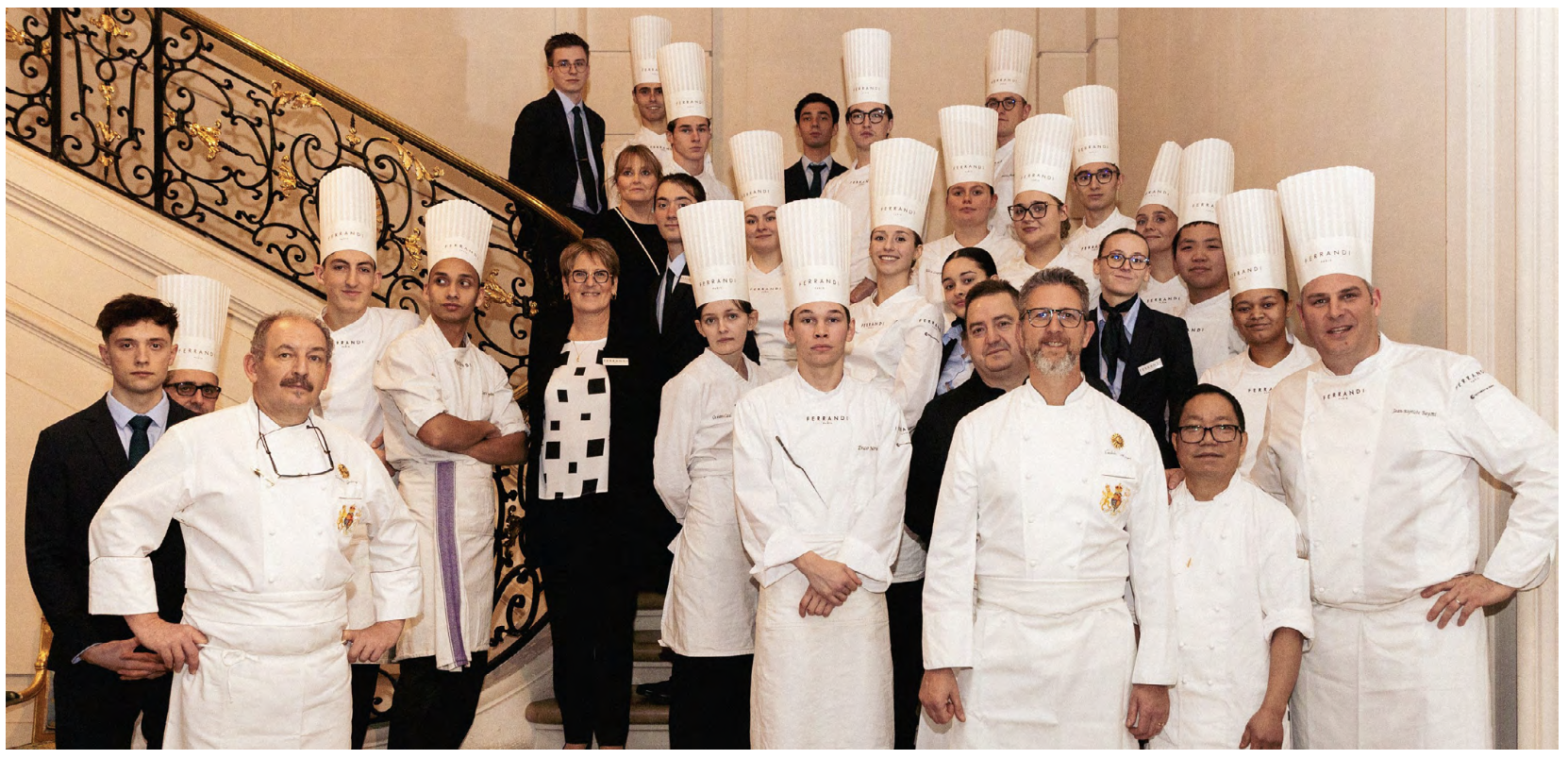 A group of chefs from Ferrandi Culinary School in white uniforms pose on a grand staircase.