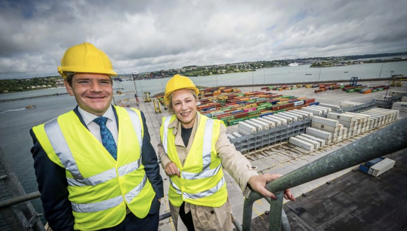 Minister Peter Burke and Minister Gillian Martin stand in yellow hard hats and high-visibility vests on a viewing platform at Port of Cork.