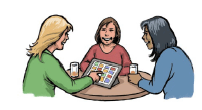 Three women sitting at a table with drinks. One woman is communicating with the others using high-tech communication equipment. All are happy and smiling.
