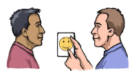 A man holding up a card and showing it to another man. The card has a happy face on it.