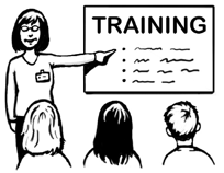 A woman wearing a name badge is pointing to a board with ‘Training’ written on it. A group of people are sitting in front of her and watching