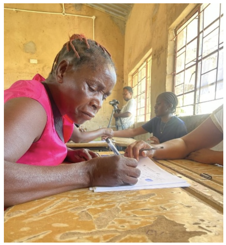 Ndubu is sat at a desk and completes a form to receive assistance.