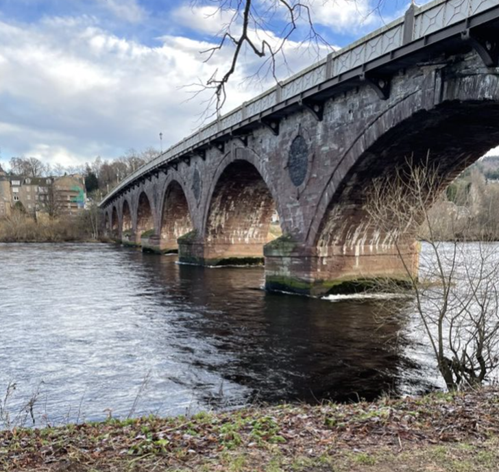 A bridge over the River Tay with trees and buildings in the background