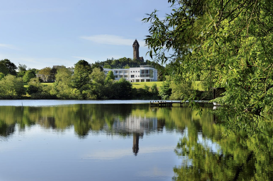 A body of water with trees and a University of Stirling building in the background.