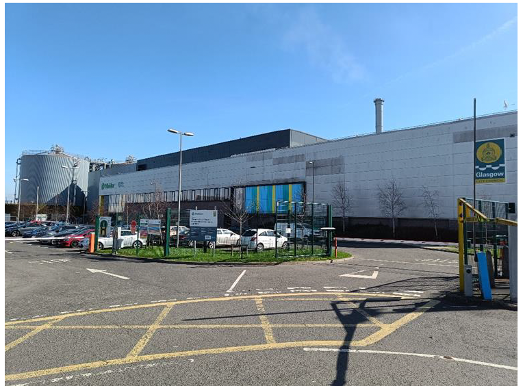 A parking lot with cars parked in front of the Glasgow Recycling building. 
