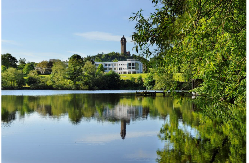 A body of water with trees and a University of Stirling building in the background.
