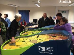 A photo taken at one of the Scottish Flood Forum’s peer to peer networking events. A man demonstrates how changes to the catchment can have an influence on flooding, using the Tweed Forum’s catchment model.
