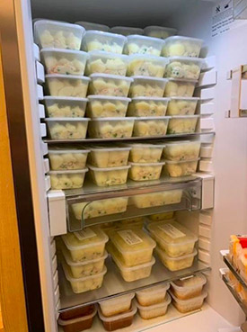 A photo of food in plastic cartons stacked up.  It is meals prepared by a local hotel owner.  