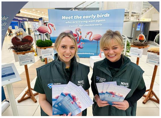 Image of two people holding campaign flyers in front of the community roadshow stand.