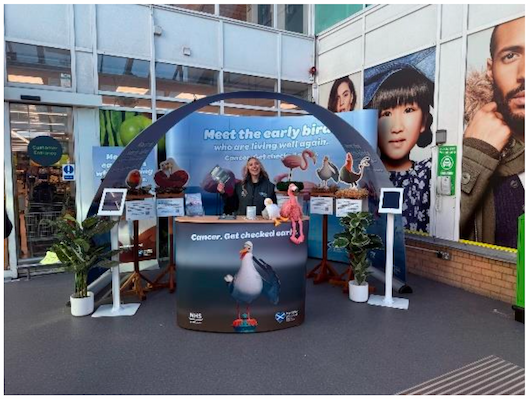 Image of a community roadshow stand at the entrance to an Asda store with a person behind the desk.
