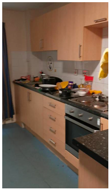 A kitchen with wooden cabinets and blue floor. There are lots of pans and dishes on the kitchen surface.