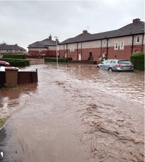 A flooded street in Tillicoultry with cars and houses. 