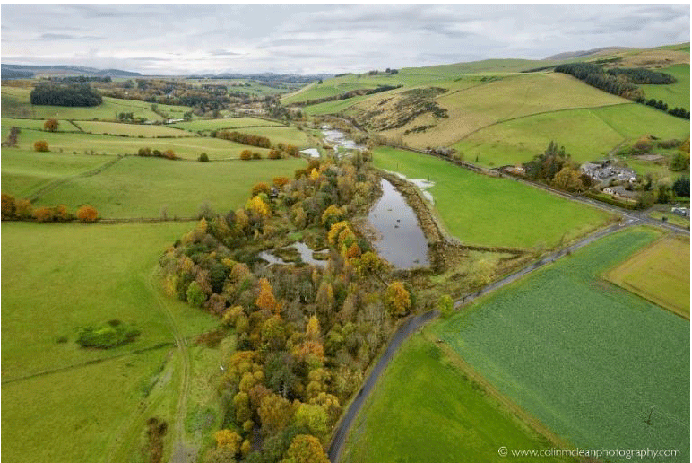 A photo of the Eddleston Water, showing a river running through a green field.