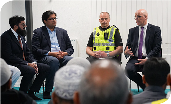 First Minister John Swinney and a police officer talk to a community group 